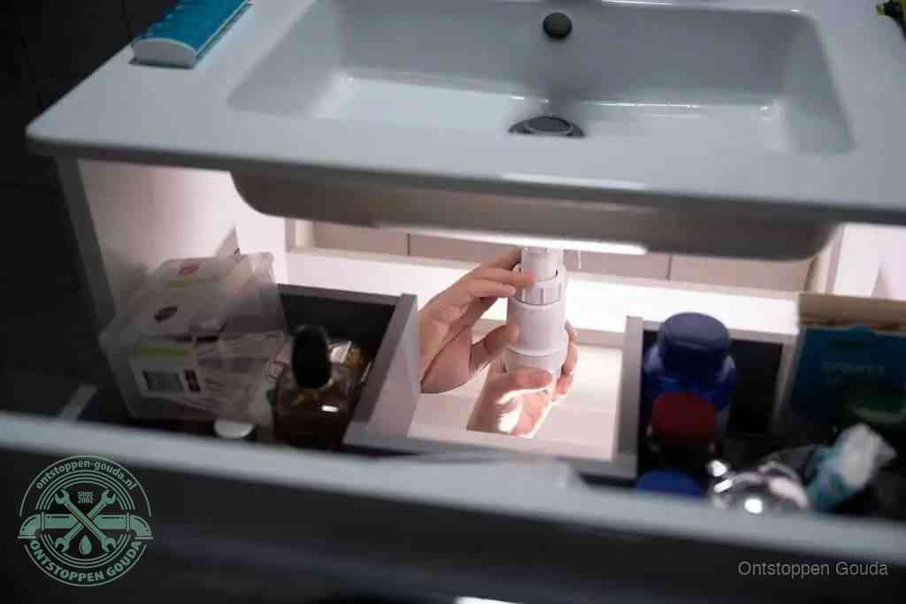 Een pompfles met zeep boven een wastafel, de heet water en afwasmiddel-methode om een vetprop in de afvoer los te maken in Gouda
