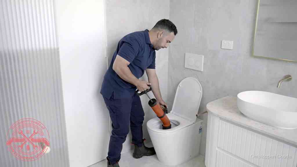 Een monteur buigt over een wandcloset en duwt met de hand een persluchtontstopper in de toiletpot om de verstopping handmatig los te maken in Gouda