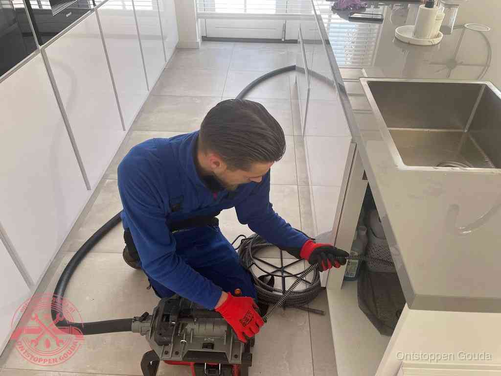 Een monteur ontstopt de keukenafvoer onder de spoelbak met een elektrische veermachine in Gouda