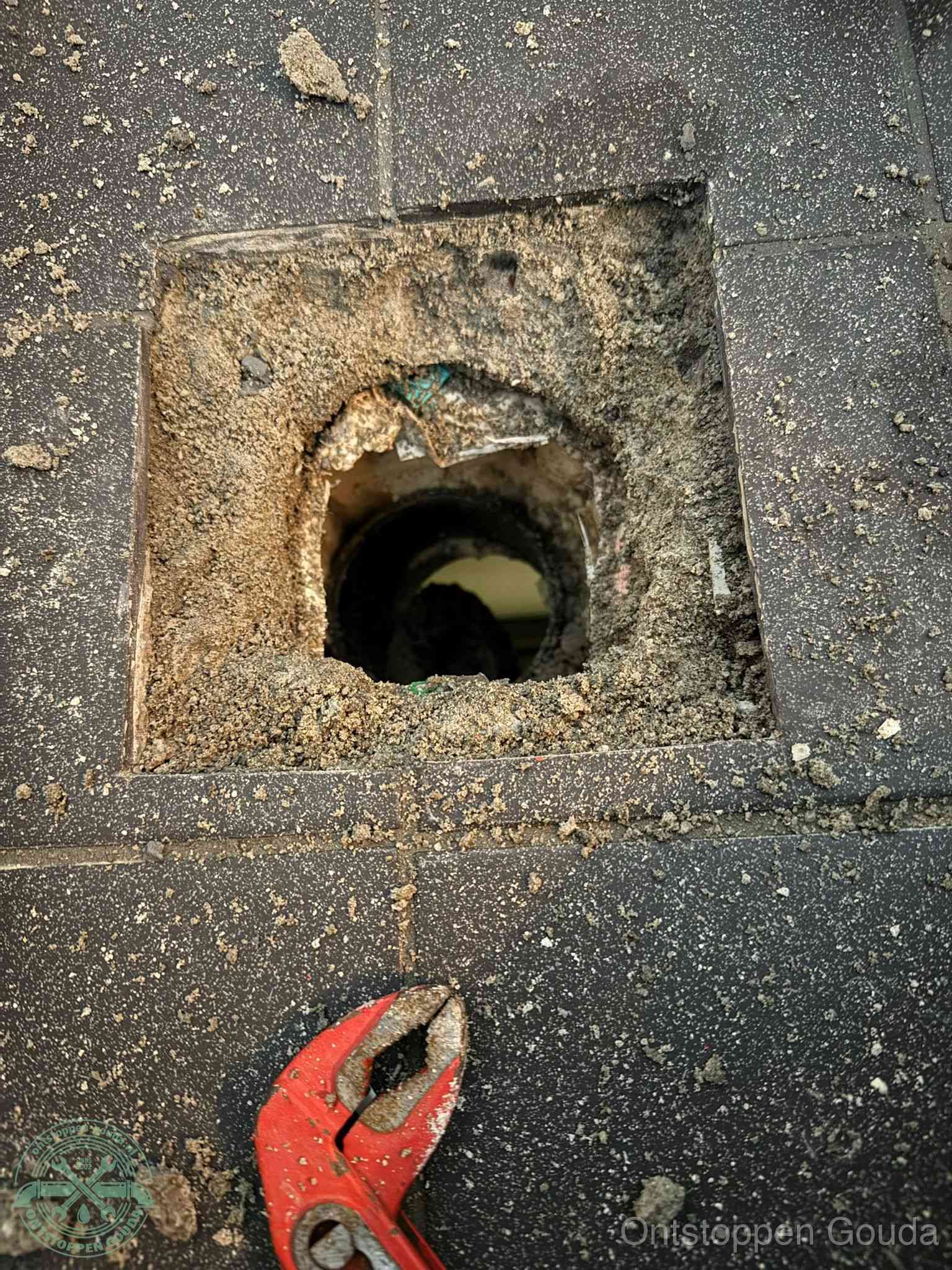 Een geopend rioolputje in een betontegelvloer met losgemaakt rooster en een zichtbare ronde afvoerbuis, het achterhalen waar de afvoerverstopping zit in Gouda