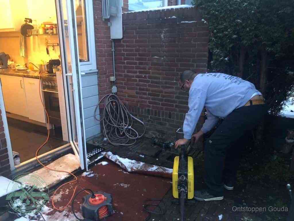 Een monteur werkt buiten bij een open riool-/grondput met een elektrische ontstoppingsmachine om een verborgen afvoerprobleem op te sporen in Gouda