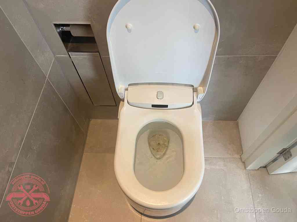 Een wit hangtoilet waarin een prop wc-papier op het water blijft drijven, een duidelijk signaal van een verstopte wc in Gouda