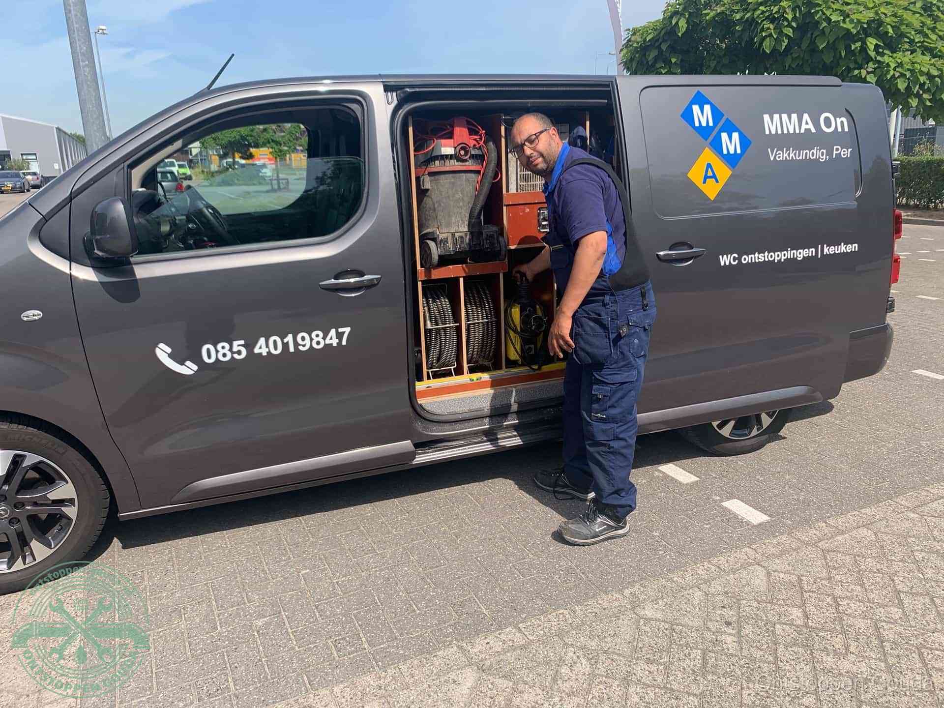 Een monteur bij de open schuifdeur van zijn bedrijfsbus op een parkeerplaats, klaar om de oorzaak van terugkerende afvoerverstoppingen aan te pakken in Gouda