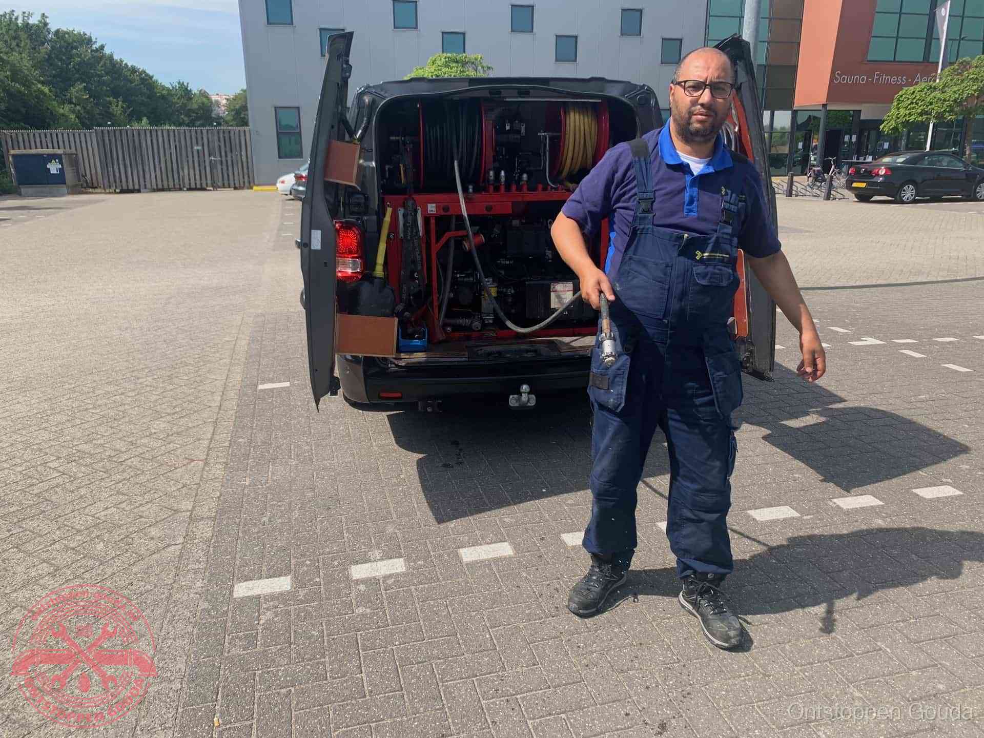Een monteur bij zijn bestelbus met een hogedruk- en rioolreinigingsunit, klaar om de oorzaak van terugkerende wc-verstoppingen aan te pakken in Gouda