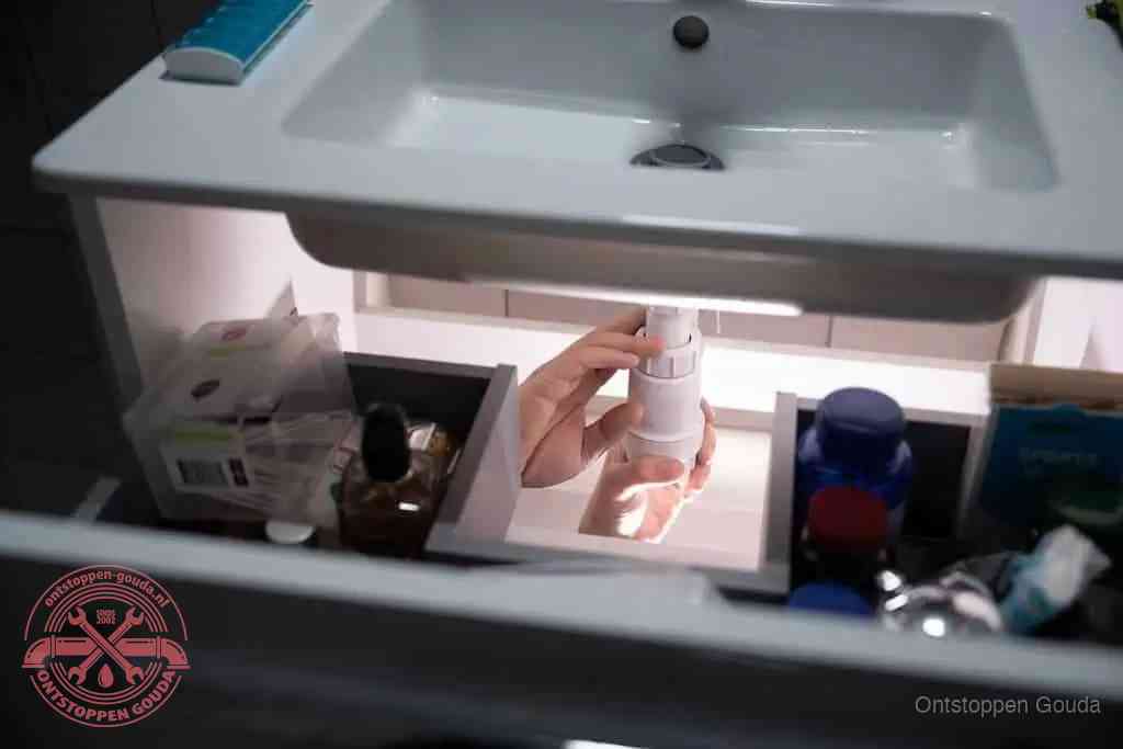 Een pompfles met zeep boven een wastafel in de toiletruimte, de warm water en afwasmiddel-methode om de wc te ontstoppen in Gouda