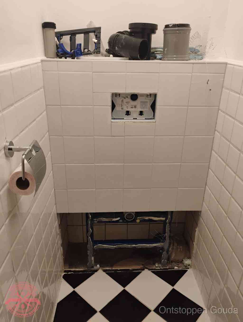 Een toiletruimte waar het hangtoilet en de inbouwreservoir-onderdelen zijn vrijgelegd voor onderhoud, periodiek nazicht voorkomt een wc-verstopping in Gouda